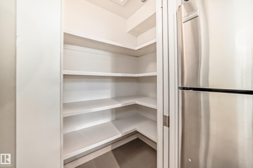 Walk-in pantry featuring white shelving, a Frigidaire stainless steel refrigerator, and dark tile flooring - 12118 125 Street Nw, Edmonton, AB - Indoor With Storage