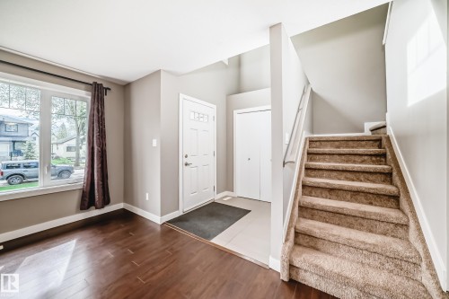 Entryway featuring wood-finish flooring, a carpeted staircase, and a white paneled front door with decorative glass inserts - 12118 125 Street Nw, Edmonton, AB - Indoor Photo Showing Other Room