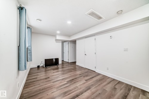 Spacious interior room featuring wood-finish flooring, white walls, recessed lighting, and multiple white panel doors - 12118 125 Street Nw, Edmonton, AB - Indoor Photo Showing Other Room