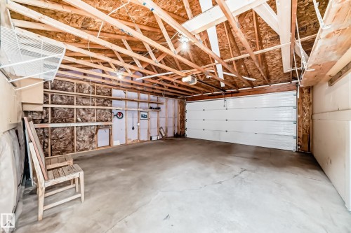 Spacious garage with a sectional overhead door, concrete flooring, and exposed wood ceiling joists - 12118 125 Street Nw, Edmonton, AB - Indoor Photo Showing Garage