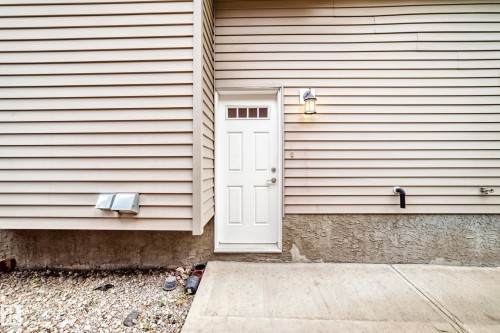 Side entrance featuring a white panel door with windows, beige siding, a wall-mounted light fixture, and a concrete pad - 12118 125 Street Nw, Edmonton, AB - Outdoor With Exterior