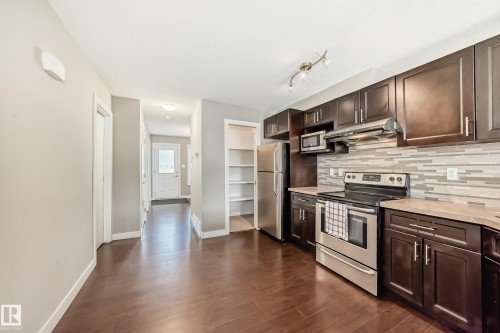 Kitchen featuring rich wood-finish flooring, dark wood cabinetry, stainless steel appliances, a tile backsplash, and light-toned countertops - 12118 125 Street Nw, Edmonton, AB - Indoor Photo Showing Kitchen
