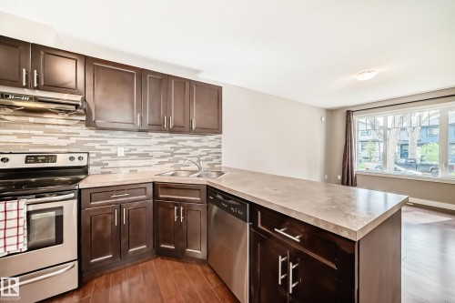 Contemporary kitchen featuring dark wood cabinetry, stainless steel appliances, and a mosaic tile backsplash - 12118 125 Street Nw, Edmonton, AB - Indoor Photo Showing Kitchen With Double Sink