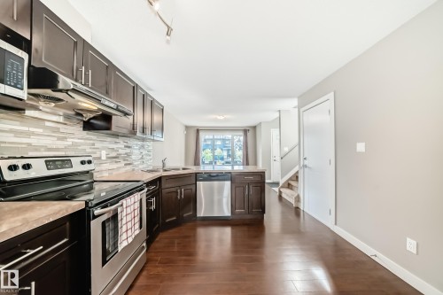 Modern kitchen featuring dark wood cabinetry, stainless steel appliances, and a mosaic tile backsplash - 12118 125 Street Nw, Edmonton, AB - Indoor Photo Showing Kitchen With Double Sink With Upgraded Kitchen