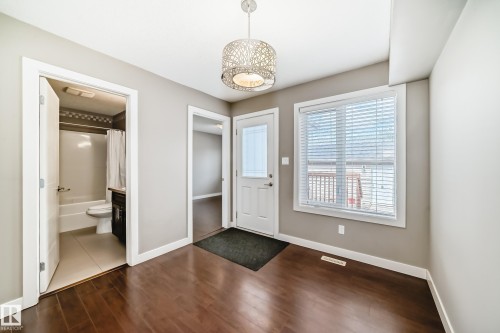 Open concept room featuring wood-finish flooring, a contemporary ceiling light fixture, a paneled door with a glass insert, and a window with horizontal blinds - 12118 125 Street Nw, Edmonton, AB - Indoor Photo Showing Other Room