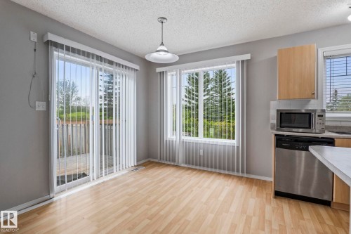 Sliding glass door to an outdoor deck, wood-finish flooring, ample natural light, stainless steel dishwasher, and built-in microwave - #80 4350 23St Nw, Edmonton, AB - Indoor Photo Showing Kitchen