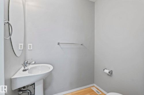 Corner pedestal sink with chrome faucet, oval wall mirror, and light wood-finish flooring - #80 4350 23St Nw, Edmonton, AB - Indoor Photo Showing Bathroom