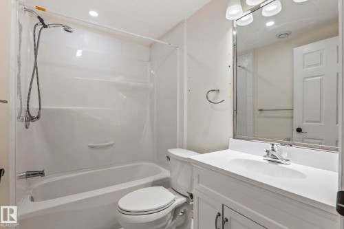 Bathtub with an integrated shower, white vanity with a single basin sink, and a framed mirror - #80 4350 23St Nw, Edmonton, AB - Indoor Photo Showing Bathroom