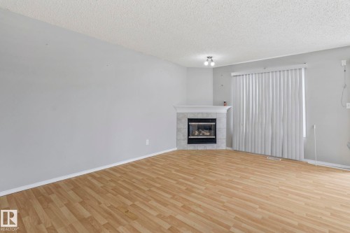 Living area featuring wood-finish flooring, a fireplace with a tiled surround, a sliding glass door, and a ceiling-mounted light fixture - #80 4350 23St Nw, Edmonton, AB - Indoor Photo Showing Living Room With Fireplace