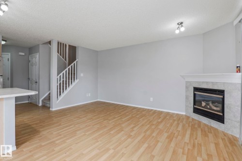 Wood-finish flooring throughout, featuring a corner fireplace with a tiled surround and mantel - #80 4350 23St Nw, Edmonton, AB - Indoor Photo Showing Living Room With Fireplace