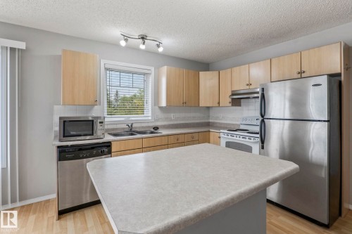 Kitchen with wood-finish cabinetry, stainless steel appliances, and a central island with a light-toned countertop - #80 4350 23St Nw, Edmonton, AB - Indoor Photo Showing Kitchen With Double Sink