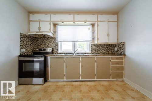 Kitchen featuring upper and lower cabinetry, mosaic tile backsplash, built-in range, and a single basin sink under a window - 7812 128 Avenue Nw, Edmonton, AB - Indoor Photo Showing Kitchen