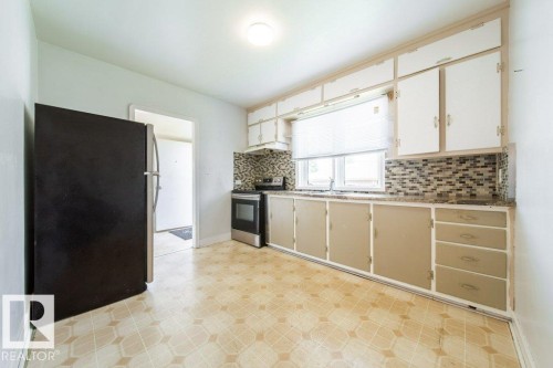 Kitchen featuring patterned flooring, mixed-material backsplash, white upper cabinetry, and a stainless steel range - 7812 128 Avenue Nw, Edmonton, AB - Indoor Photo Showing Kitchen