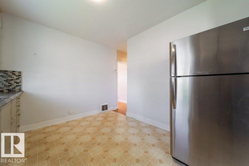 Stainless steel refrigerator, mosaic tile backsplash, light-toned cabinetry, and patterned flooring - 7812 128 Avenue Nw, Edmonton, AB - Indoor