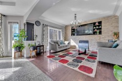 Hardwood flooring, natural light through large windows, a stacked stone accent wall with integrated shelving, a built-in fireplace, and an elegant chandelier - 