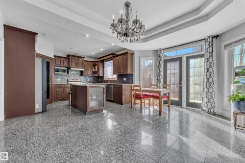 Kitchen featuring dark wood cabinetry, a central island with glass-front storage, stainless steel appliances, and tile flooring - 10915 175 Avenue Nw, Edmonton, AB - Indoor