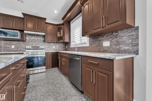 Brown cabinetry featuring brushed brass hardware, stainless steel appliances, light-toned countertops, and a full-height tile backsplash - 10915 175 Avenue Nw, Edmonton, AB - Indoor Photo Showing Kitchen With Upgraded Kitchen