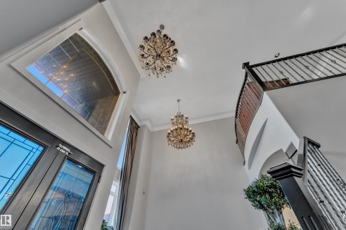 Two-story foyer featuring two chandeliers, a grand staircase with wrought iron balusters, and transom windows - 10915 175 Avenue Nw, Edmonton, AB - Indoor Photo Showing Other Room