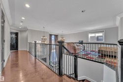 Upper-level landing with wood-finish flooring, recessed lighting, and an ornate wrought-iron railing overlooking the lower level - 