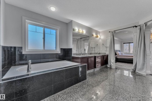 Built-in soaking tub with black tile surround, dual vanity with granite countertops, dark wood-finish cabinetry, and polished tile flooring - 10915 175 Avenue Nw, Edmonton, AB - Indoor Photo Showing Bathroom