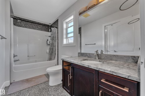 Bathroom featuring a single vanity with an integrated sink, stone countertop, dark wood-finish cabinetry with bar pull hardware, and a tub/shower combination with a textured tile surround - 10915 175 Avenue Nw, Edmonton, AB - Indoor Photo Showing Bathroom