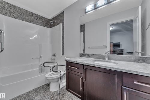 Tub/shower combination with a textured surround, single vanity with a stone countertop, integrated sink, and dark wood-finish cabinetry - 10915 175 Avenue Nw, Edmonton, AB - Indoor Photo Showing Bathroom