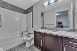 Tub/shower combination with a textured surround, single vanity with a stone countertop, integrated sink, and dark wood-finish cabinetry - 