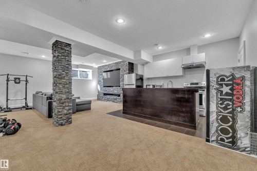 Recessed lighting throughout, stone-clad pillar, built-in media wall with stone surround, compact kitchen area with white cabinetry, and a dark wood-finish breakfast bar - 10915 175 Avenue Nw, Edmonton, AB - Indoor Photo Showing Other Room
