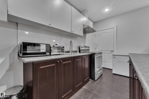 Kitchen featuring wood-finish lower cabinetry, white upper cabinetry, tiled backsplash, and recessed lighting - 10915 175 Avenue Nw, Edmonton, AB - Indoor Photo Showing Kitchen With Upgraded Kitchen