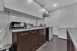 Kitchen featuring wood-finish lower cabinetry, white upper cabinetry, tiled backsplash, and recessed lighting - 
