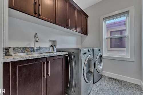 Built-in cabinetry with a sink, stone countertop, upper storage cabinets, and a window - 10915 175 Avenue Nw, Edmonton, AB - Indoor Photo Showing Laundry Room