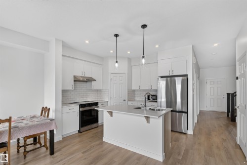 Kitchen featuring an island with an undermount sink, stainless steel appliances, and white shaker cabinetry - 1676 27 Street Nw, Edmonton, AB 