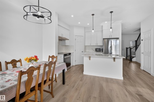 White shaker cabinetry, stainless steel appliances, pendant lighting, wood-finish flooring, and a white subway tile backsplash - 1676 27 Street Nw, Edmonton, AB 