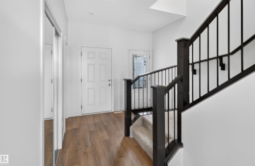 Wood-finish flooring, white paneled door, black metal railings, and carpeted stairs - 1676 27 Street Nw, Edmonton, AB 