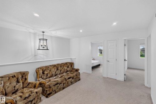 Carpeted open area with recessed lighting, a contemporary black metal chandelier, and white paneled doors - 1676 27 Street Nw, Edmonton, AB 