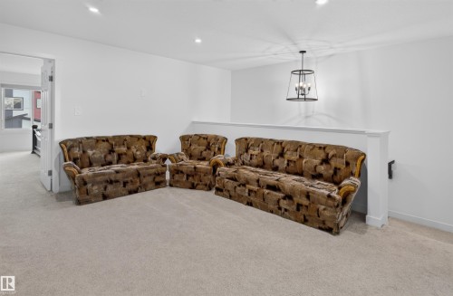 Carpeted room featuring a white interior wall, a decorative railing, and an overhead drum pendant light - 1676 27 Street Nw, Edmonton, AB 
