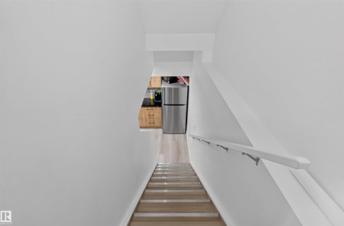 Staircase with a wall-mounted handrail, wood-finish flooring, and light wall finishes - 1676 27 Street Nw, Edmonton, AB 