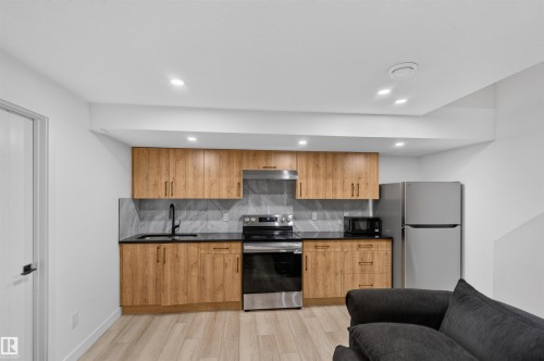Wood-finish cabinetry paired with dark countertops and a geometric tile backsplash - 1676 27 Street Nw, Edmonton, AB 