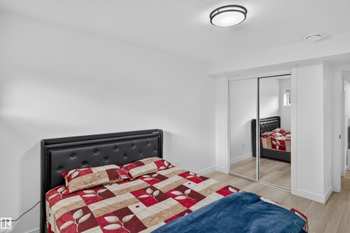 Bright bedroom featuring wood-finish flooring, mirrored sliding closet doors, and a flush-mount ceiling light fixture - 1676 27 Street Nw, Edmonton, AB 