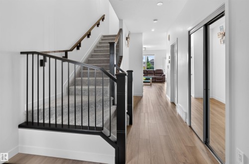 Carpeted staircase with black iron railings, wood-finish flooring throughout, and mirrored closet doors - 1676 27 Street Nw, Edmonton, AB 