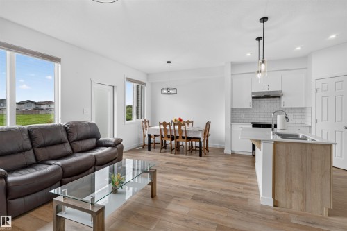 Open-concept living space featuring wood-finish flooring, white walls, and contemporary lighting fixtures - 1676 27 Street Nw, Edmonton, AB 