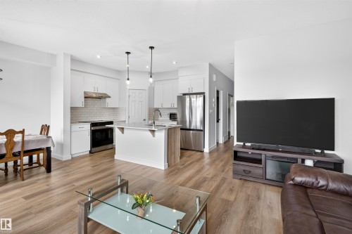 Open-concept living space featuring wood-finish flooring, recessed lighting, and a kitchen with white cabinetry, stainless steel appliances, and a tiled backsplash - 1676 27 Street Nw, Edmonton, AB 