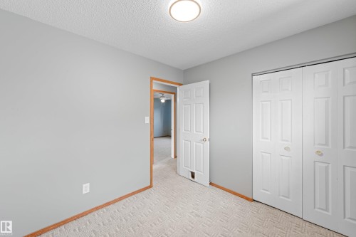 Neutral gray wall paint, patterned carpeting, natural wood trim, overhead flush-mount lighting, and bi-fold closet doors - 14538 37 Street Nw, Edmonton, AB 