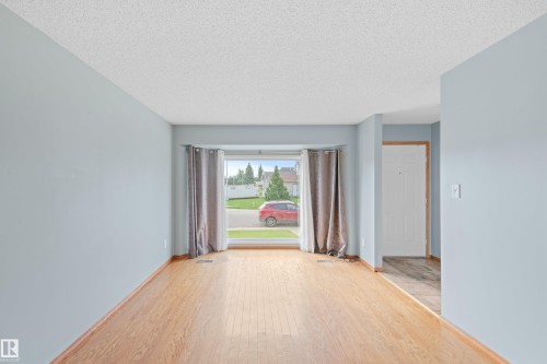 Hardwood-style flooring throughout, bay window with light-filtering curtains, and a white paneled door - 14538 37 Street Nw, Edmonton, AB 