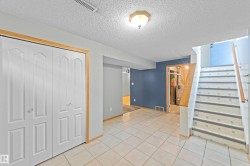 Tile flooring extending into a spacious area with bi-fold closet doors, a built-in ceiling light fixture, and an open staircase with a wood handrail - 