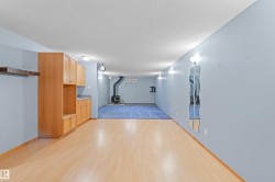 Spacious room with wood-finish flooring, built-in wooden cabinetry, recessed lighting, wall sconces, and a wood-burning stove with a black stovepipe - 