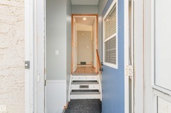 Entryway featuring a blue door with an integrated window, wood-finish handrail, and carpeted steps - 