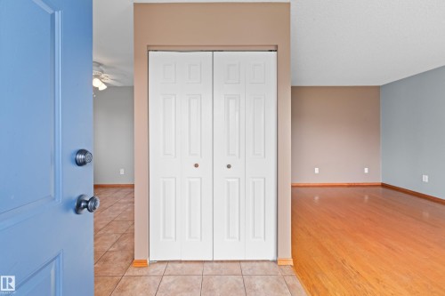 Entryway featuring tile flooring, a bi-fold closet, and a light blue door, opening to a room with wood-finish flooring and a ceiling fan - 14538 37 Street Nw, Edmonton, AB 