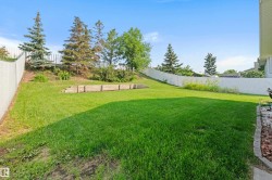 Expansive grassy yard with tiered landscaping, surrounded by a white privacy fence - 