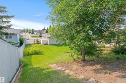 Expansive backyard with a manicured lawn, mature trees, and chain-link fencing - 